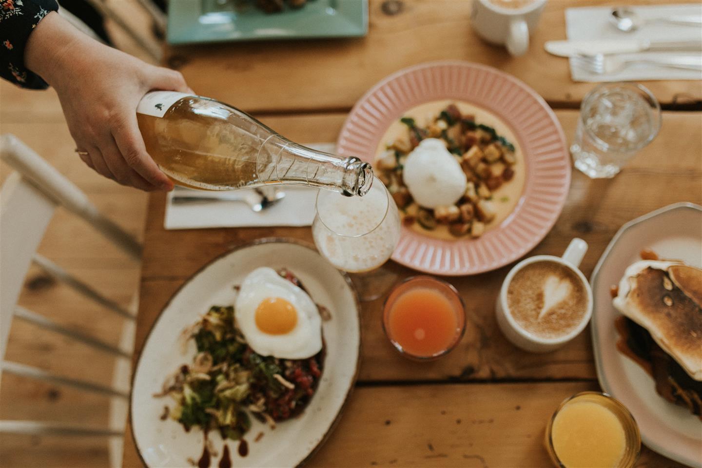 Une personne verse du mousseux dans un verre à vin sur une table brunch