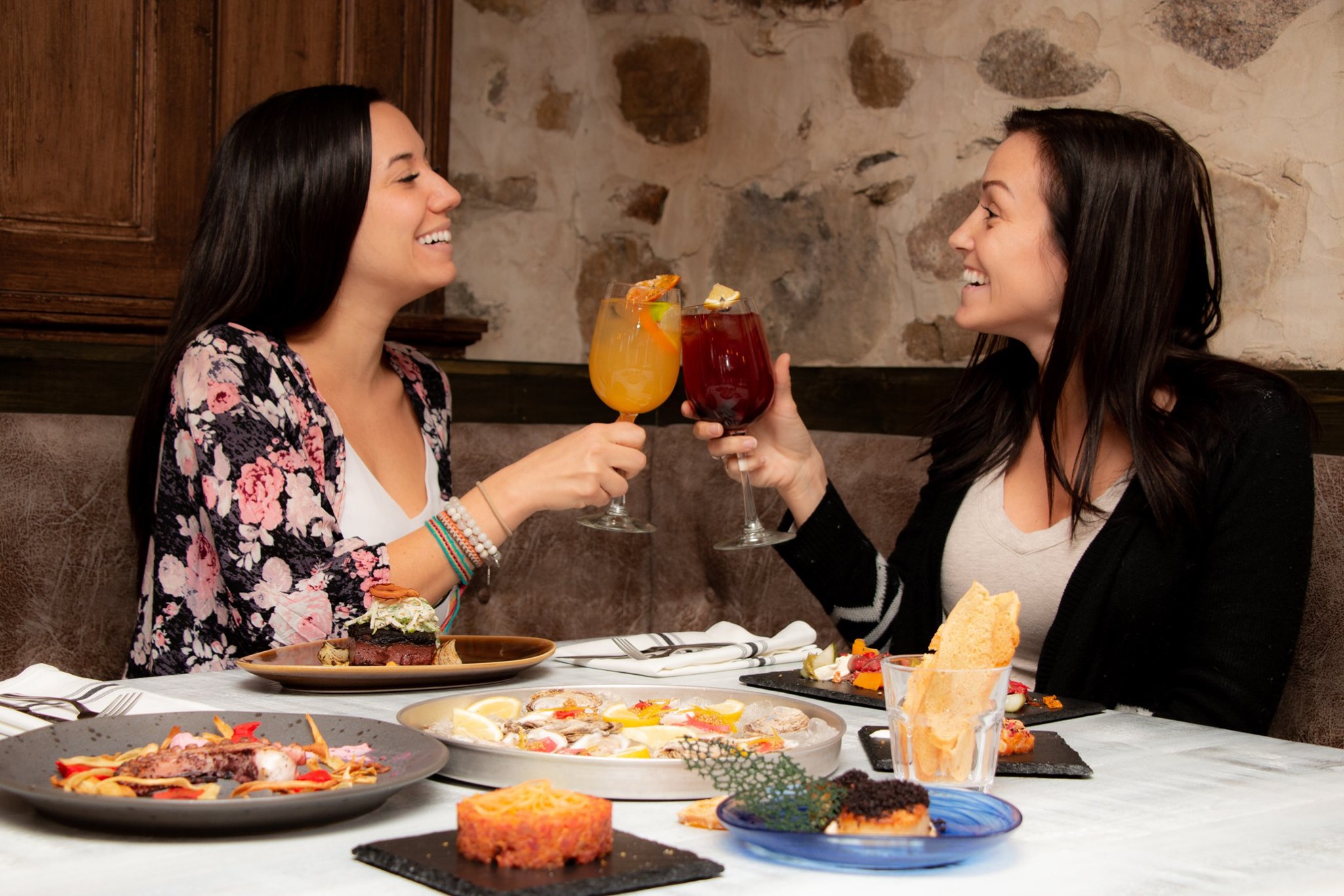 Deux femmes lèvent leurs verres devant plusieurs plats du Vice-Caché